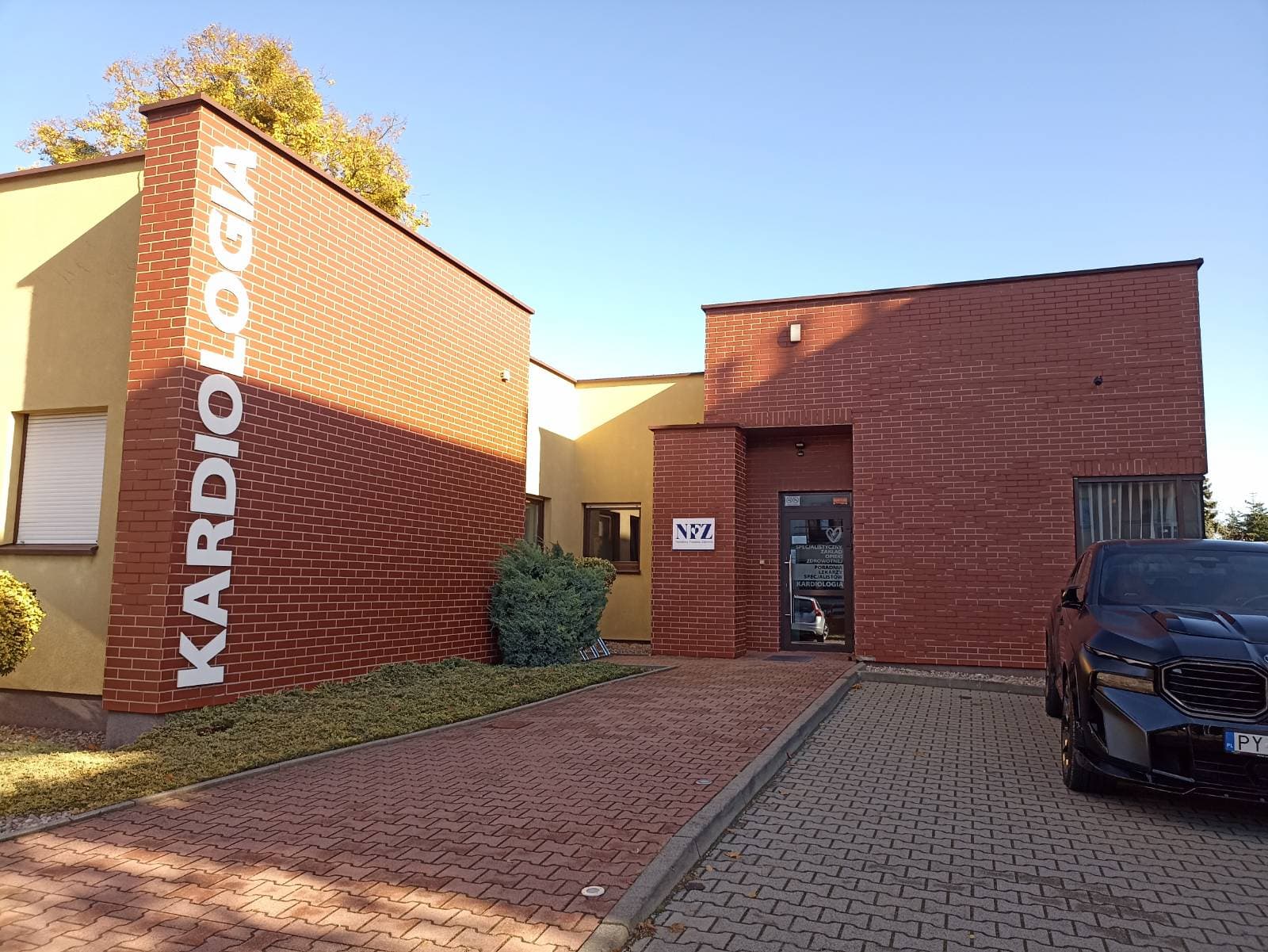 Wejście do budynku przy ul. Piłsudskiego 7A — przeszklone drzwi w ceglanej części budynku z napisem „Kardiologia”